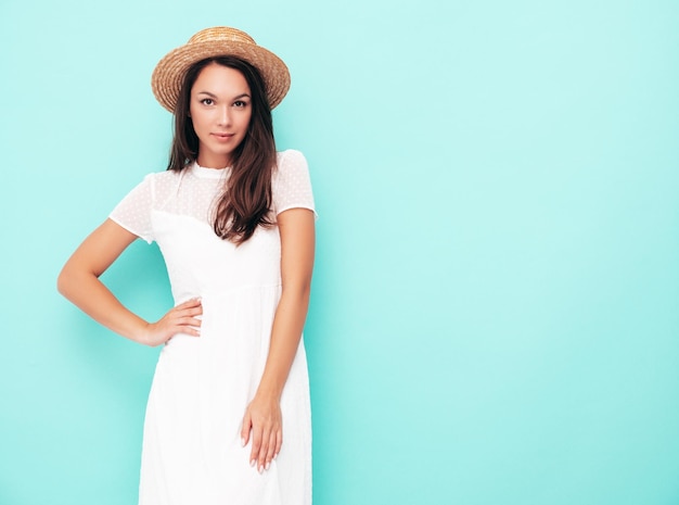 Junge schöne lächelnde Frau in trendiger Sommerkleidung Sexy sorglose Frau posiert in der Nähe der blauen Wand im Studio Positives brünettes Modell, das Spaß hat Fröhlich und glücklich In Hut