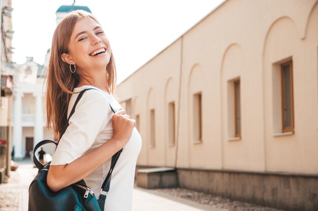 Junge schöne lächelnde Hipster-Frau im trendigen Sommerkleid Sexy sorglose Frau, die bei Sonnenuntergang auf dem Straßenhintergrund posiert Positives Modell im Freien Fröhlich und glücklich mit Handtasche