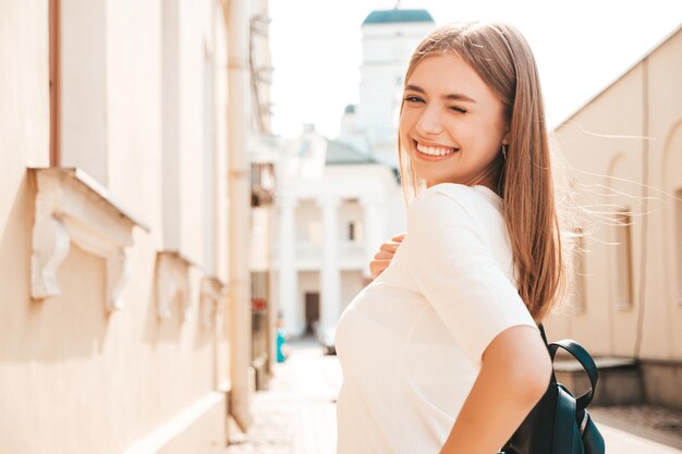 Junge schöne lächelnde Hipster-Frau im trendigen Sommerkleid Sexy sorglose Frau, die bei Sonnenuntergang auf der Straße im Hintergrund posiert Positives Modell, das im Freien lacht Fröhlich und glücklich Zwinkert