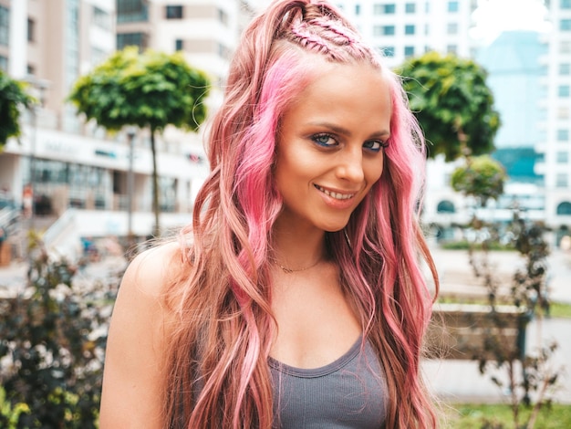 Junge schöne lächelnde Hipster-Frau in trendigen Sommer-Jeans-Shorts mit rosa Frisur. Sexy sorgloses Model posiert auf der Straße. Positives Modell im Freien. Fröhlich und glücklich