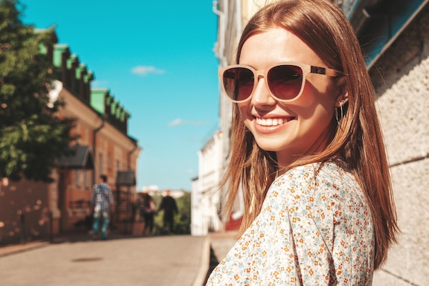 Junge schöne lächelnde Hipster-Frau in trendiger Sommerkleidung Sexy sorglose Frau, die bei Sonnenuntergang auf dem Straßenhintergrund posiert Positives Modell im Freien Fröhlich und glücklich mit Sonnenbrille