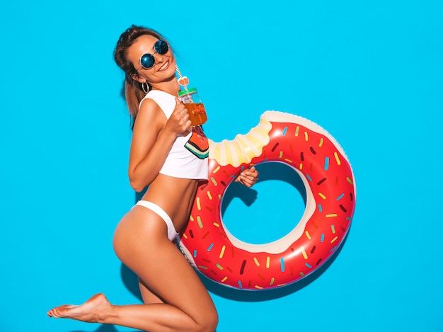 Junge schöne lächelnde sexy Frau in der Sonnenbrille. Mädchen in den weißen Sommerunterhosen und -thema mit aufblasbarer Matratze des Donut lilo. . Frisches Cocktail smoozy Getränk trinken