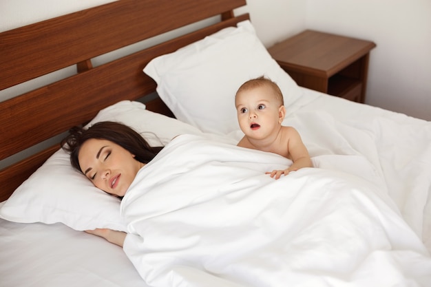 Junge schöne Mutter und ihr neugeborenes Baby liegend am frühen Morgen im Bett schlafend.