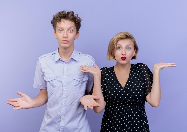 Junge schöne Paar Mann und Frau verwirrt Achselzucken Schultern ohne Antwort über blaue Wand stehen
