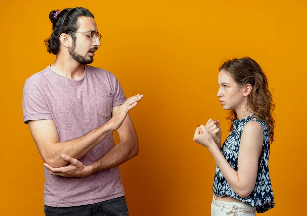 junge schöne Paare Mann und Frau streiten und gestikulieren und schauen sich mit stirnrunzelnden Gesichtern an, die über orange Wand stehen