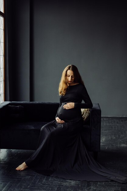 Junge schöne schwangere Frau im schwarzen Kleid Schwangerschaftsmode-Lookkonzept