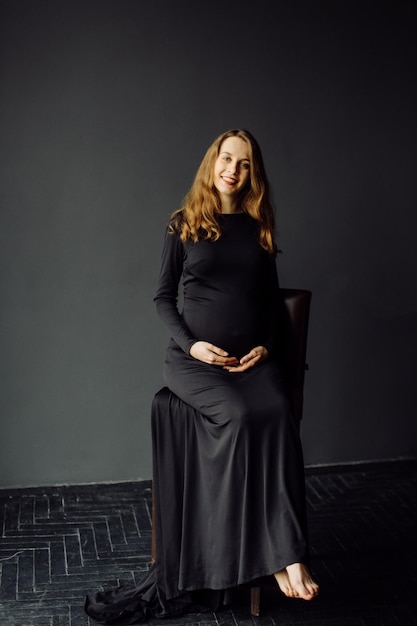 Junge schöne schwangere Frau im schwarzen Kleid Schwangerschaftsmode-Lookkonzept