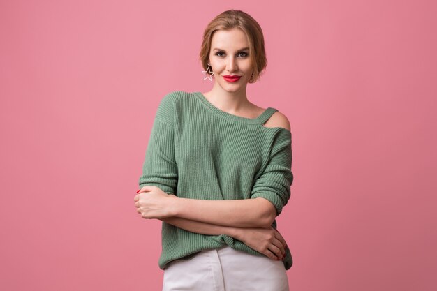 Junge schöne selbstbewusste Frau, rote Lippen, sexy Blick, grüner lässiger Pullover, verschränkte Arme, stilvoll, Modell, das im Studio aufwirft, isoliert, rosa Hintergrund, in der Kamera schauend