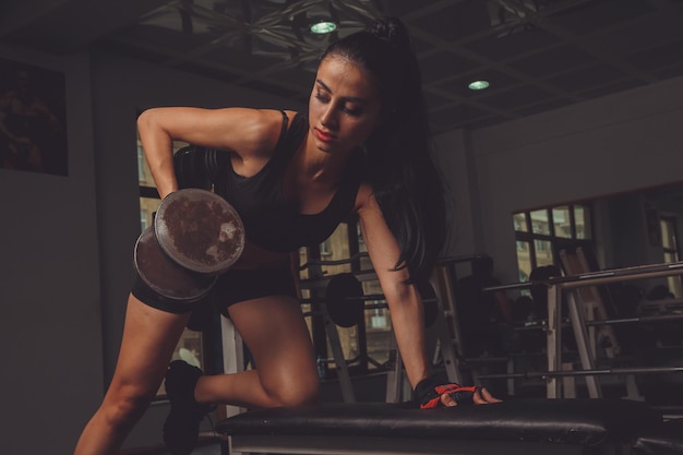 Junge schöne sexy blonde Sportlerin trainiert im Fitnessstudio in schöner Sportbekleidung auf dunklem Hintergrund