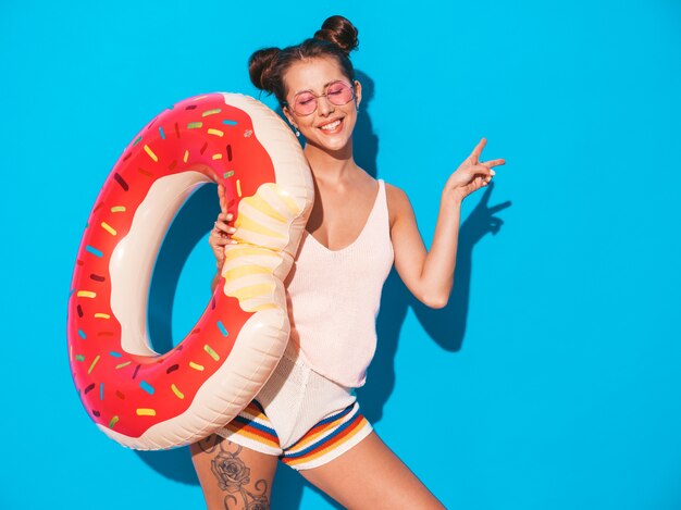 Junge schöne sexy lächelnde Hippie-Frau in der Sonnenbrille. mit Krapfen lilo aufblasbare Matratze. Zeigt Friedenszeichen