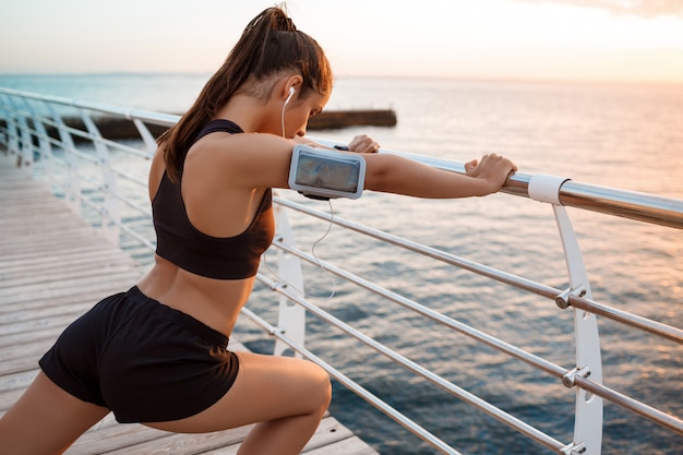 Junge schöne sportliche Mädchenausbildung bei Sonnenaufgang über dem Meer.