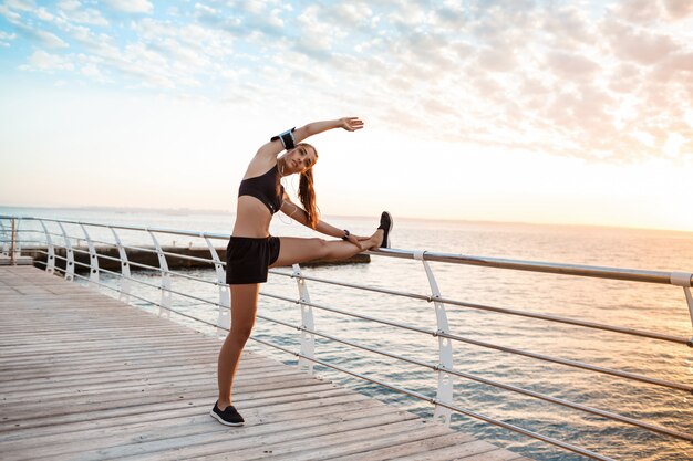 Junge schöne sportliche Mädchenausbildung bei Sonnenaufgang über dem Meer.