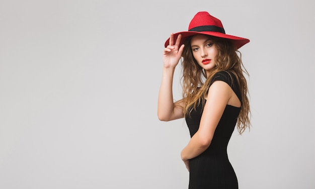 Junge schöne stilvolle Frau im schwarzen Kleid, im roten Hut, im roten Lippenstift, glücklich, lächelnd, sexy, elegant