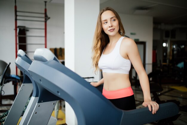 Junge Schönheitsfrau, die auf Laufsimulator im Sportgymnastikclub ausarbeitet.