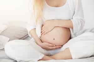 Kostenloses Foto junge schwangere bald mutter sein, die ihren bauch berührt, der am nachmittag in ihrem schlafzimmer sitzt. schwangerschaftskonzept.