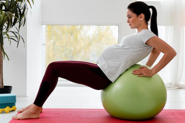 Junge schwangere Frau der Seitenansicht, die auf Fitnessball ausübt