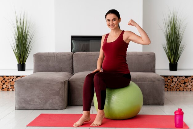 Junge schwangere Frau der Vorderansicht, die einen Fitnessball verwendet