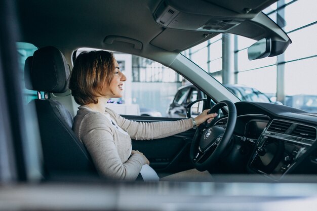 Junge schwangere Frau, die ein Auto im Autoausstellungsraum testend