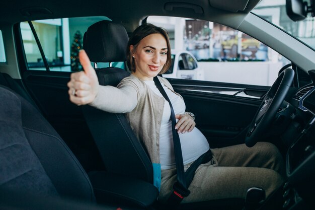 Junge schwangere Frau, die ein Auto im Autoausstellungsraum testend