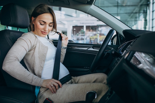 Junge schwangere Frau, die ein Auto im Autoausstellungsraum testend