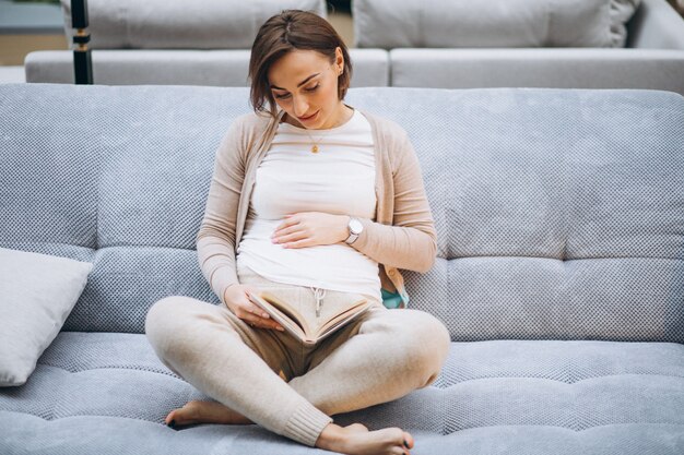 Junge schwangere Frau, die ein Buch zu Hause liest