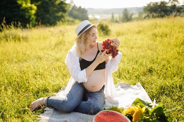 Junge schwangere Frau, die im Park draußen entspannt und Wassermelone isst, gesunde Schwangerschaft