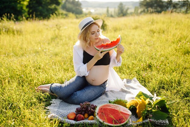 Junge schwangere Frau, die im Park draußen entspannt und Wassermelone isst, gesunde Schwangerschaft