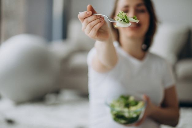 Junge schwangere frau, die salat zu hause isst