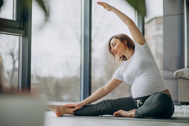 Junge schwangere Frau, die Yoga zu Hause praktiziert