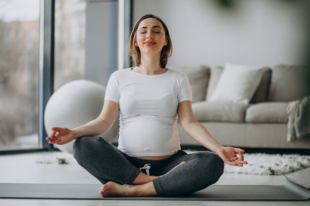 Junge schwangere Frau, die Yoga zu Hause praktiziert