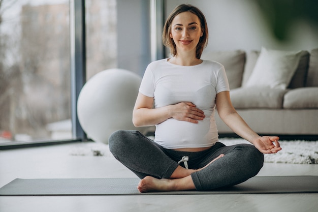 Junge schwangere Frau, die Yoga zu Hause praktiziert