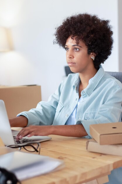 Junge schwarze Frau sitzt am Schreibtisch und arbeitet zu Hause am Computer. Kurzhaarige Dame, die auf den Computerbildschirm blickt und sich auf die Lösung der täglichen Arbeitsaufgaben konzentriert. Kleinunternehmen, Bürokonzept