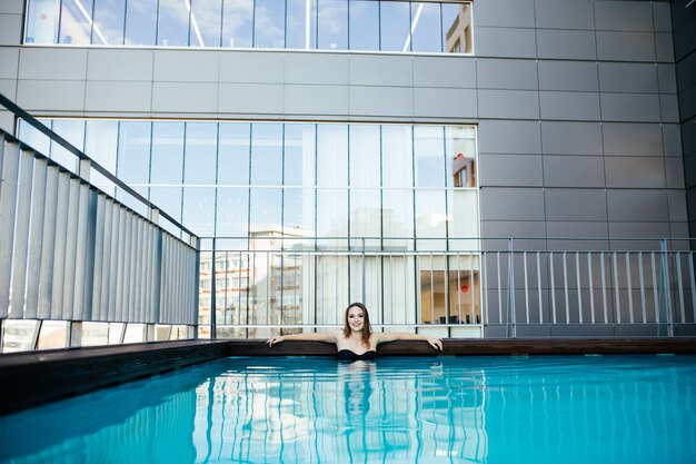 Junge sexy Frau, die im Wasser an einem Pool im sonnigen heißen Tag entspannt