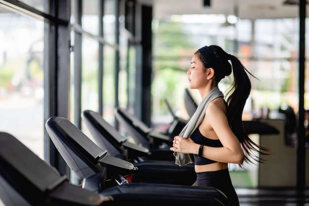 Junge sexy Frau mit Sportbekleidung, schweißfestem Stoff und Smartwatch, die auf dem Laufband läuft, um im modernen Fitnessstudio zu trainieren, zu lächeln, Platz zu kopieren