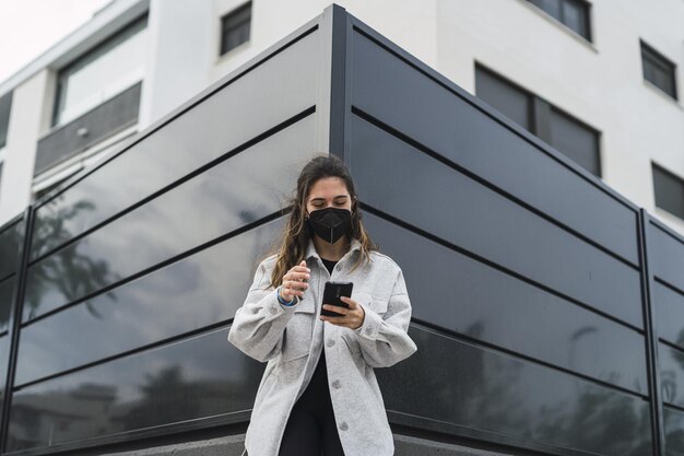 Junge Spanierin mit schwarzer Gesichtsmaske macht einen Videoanruf, während sie sich draußen ausruht