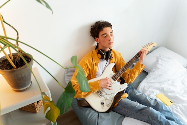 Kostenloses Foto junge spielt gitarre im innenbereich hoher winkel