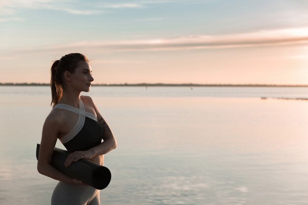 Junge Sportfrau am Strand, der mit Teppich steht