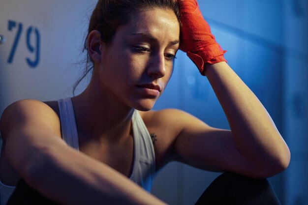 Junge Sportlerin fühlt sich nicht motiviert, während sie vor dem Sporttraining in der Umkleidekabine des Fitnessstudios sitzt