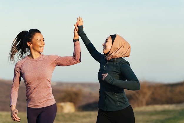 Junge Sportlerin und ihr Personal Trainer haben Spaß beim Laufen und geben sich in der Natur Highfive