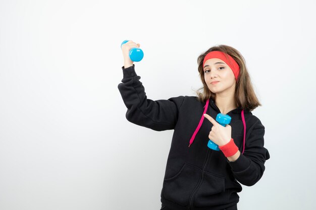 Junge sportliche Frau, die blaue Hanteln steht und hält. Foto in hoher Qualität