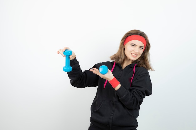 Junge sportliche Frau, die blaue Hanteln steht und hält. Foto in hoher Qualität