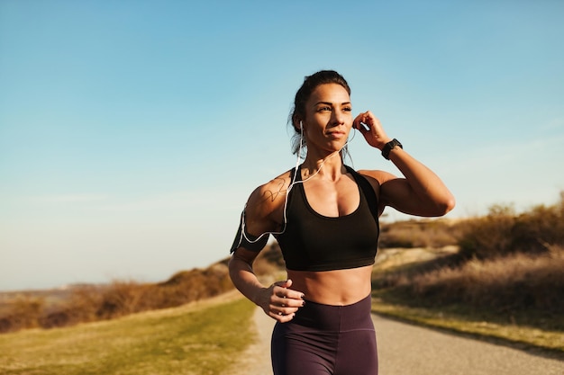 Junge sportliche Frau, die Musik über Kopfhörer hört, während sie in der Natur joggt Platz kopieren