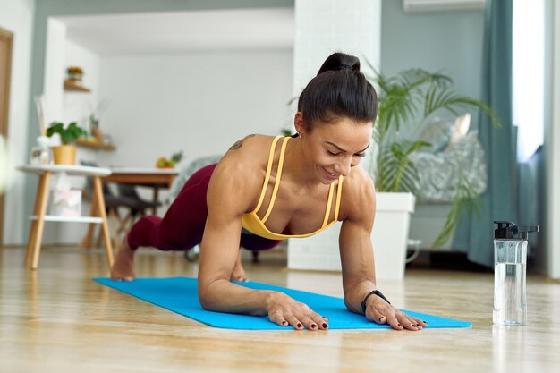 Junge sportliche Frau in Plankenhaltung, die im Wohnzimmer trainiert