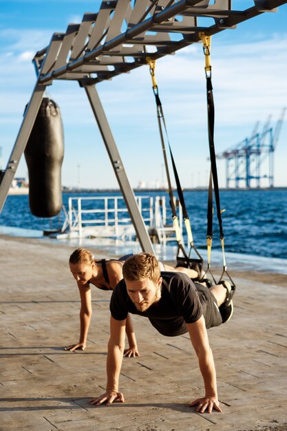 Junge sportliche Leute, die mit trx nahe Meer am Morgen trainieren.