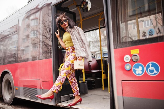 Junge stilvolle afrikanisch-amerikanische Frau mit moderner Sonnenbrille, die in einem Bus fährt