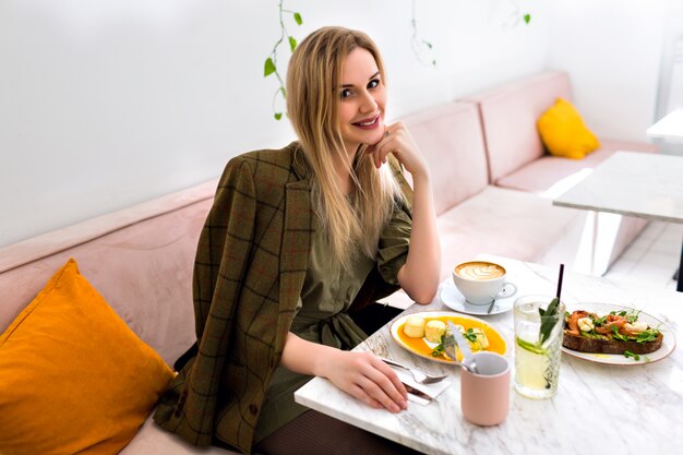 Junge stilvolle elegante Frau, die ihr leckeres Frühstück im stilvollen Hipster-Café, Morgenzeit, elegantes Outfit genießt.