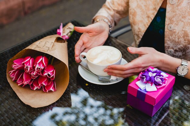 Junge stilvolle Frau, die im Café sitzt und Tasse Cappuccino hält