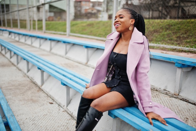 Junge stilvolle schöne afrikanisch-amerikanische Frau auf der Straße an den Stadiontribünen mit Mode-Outfit-Mantel