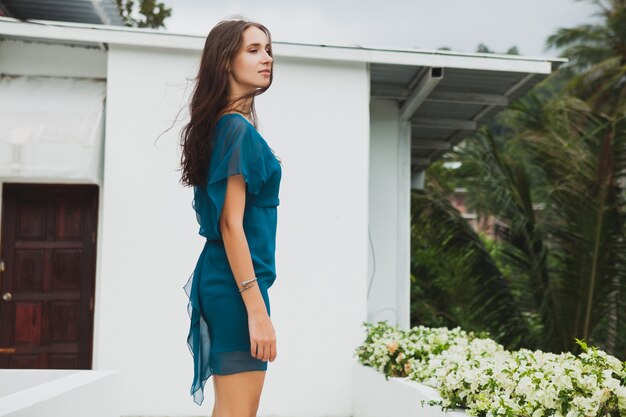 Junge stilvolle schöne Frau im blauen Kleid, Sommermodetrend, Urlaub, Garten, tropische Hotelterrasse, lächelnd, gehend