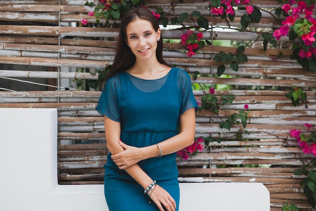 Junge stilvolle schöne Frau im blauen Kleid, Sommermodetrend, Urlaub, Garten, tropische Hotelterrasse, lächelnd